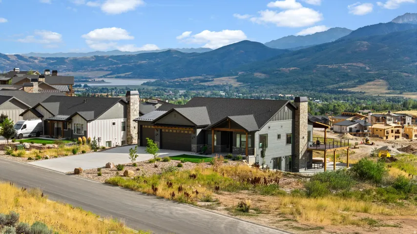 Modern farmhouse-style architecture with an attached two-car garage, stone and siding exterior, expansive outdoor deck, and a multi-pitch roofline