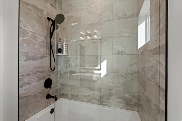 Bathtub and shower combination with full-height tile surround, matte black fixtures, and a recessed shower niche