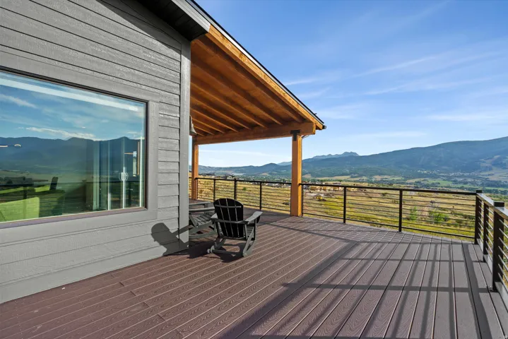 Expansive outdoor deck with composite decking and metal railings, featuring a large window and a covered patio with exposed wood beams