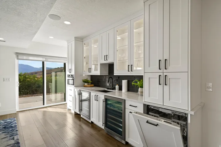 White cabinetry with black hardware, wood-finish flooring, built-in microwave, integrated dishwasher, and a glass sliding door
