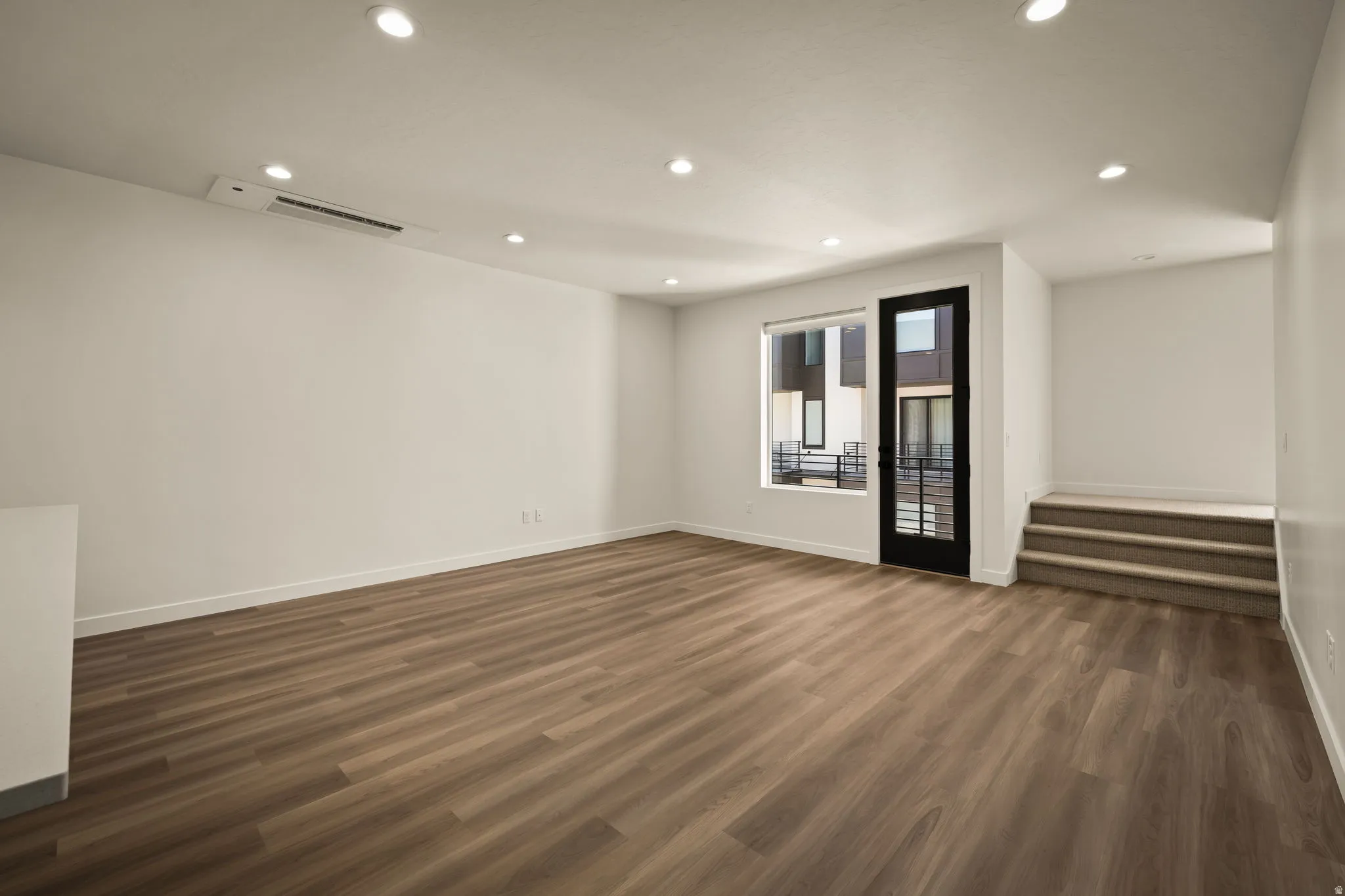 Wood-finish flooring throughout, recessed ceiling lighting, a dark-framed glass door, and a white interior