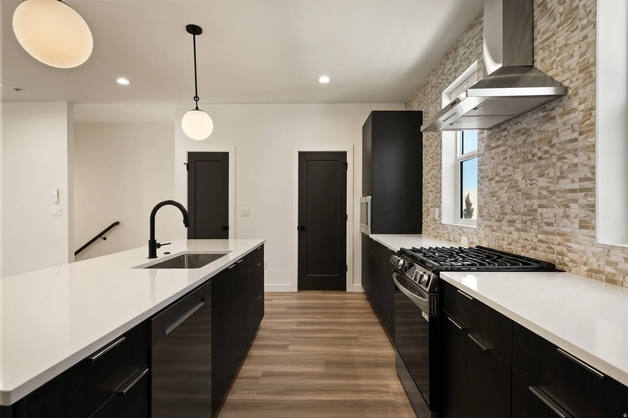 Modern kitchen featuring dark cabinetry, light countertops, wood-finish flooring, a stainless steel range hood, and a gas range