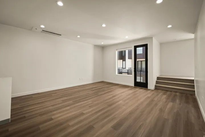 Wood-finish flooring throughout, recessed ceiling lighting, a dark-framed glass door, and a white interior