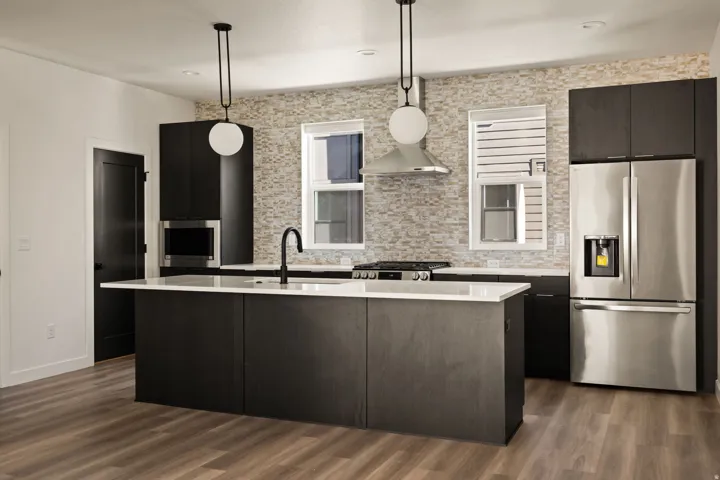 Modern kitchen featuring an expansive center island, integrated stainless steel appliances, dark wood-finish cabinetry, a textured tile backsplash, and wood-finish flooring