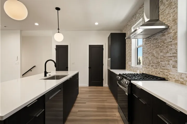 Modern kitchen featuring dark cabinetry, light countertops, wood-finish flooring, a stainless steel range hood, and a gas range