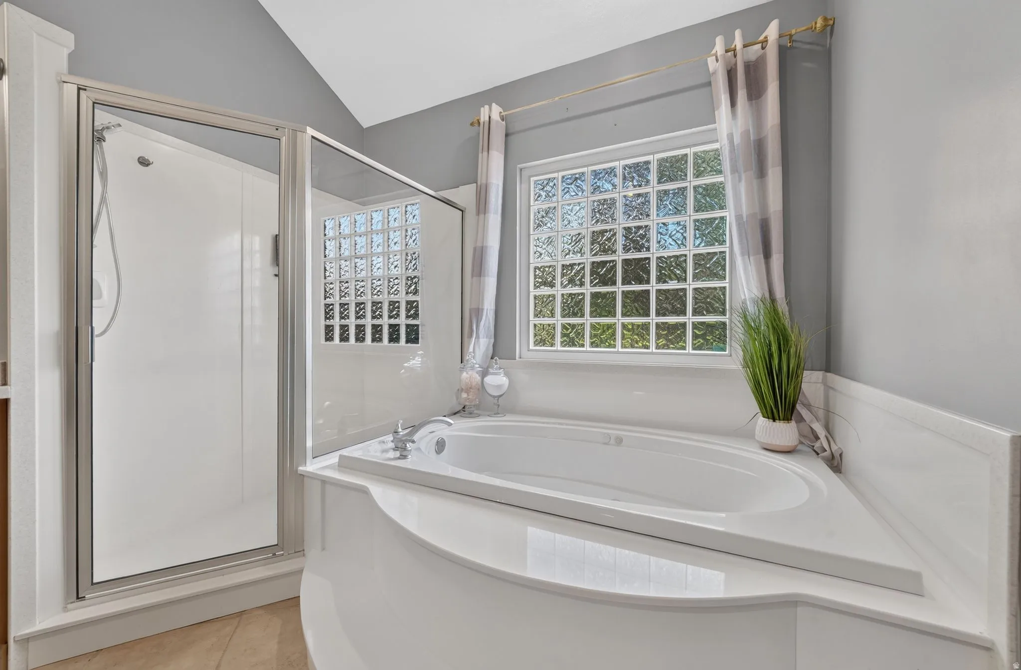 Built-in corner soaking tub with a surrounding tiled deck, framed glass block window, and a separate glass-enclosed shower
