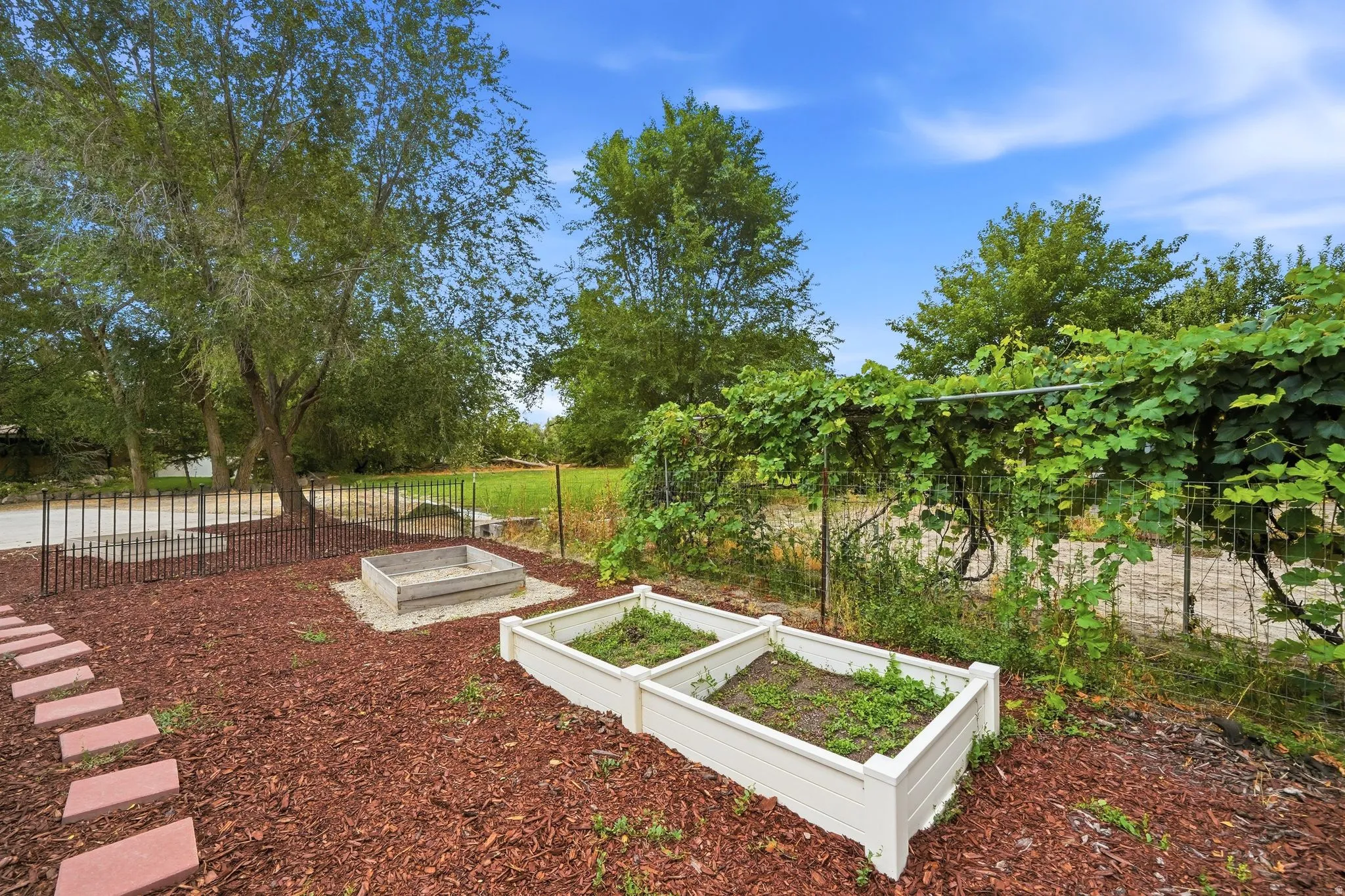 Landscaped yard with raised garden beds, a fire pit area, and a decorative metal fence