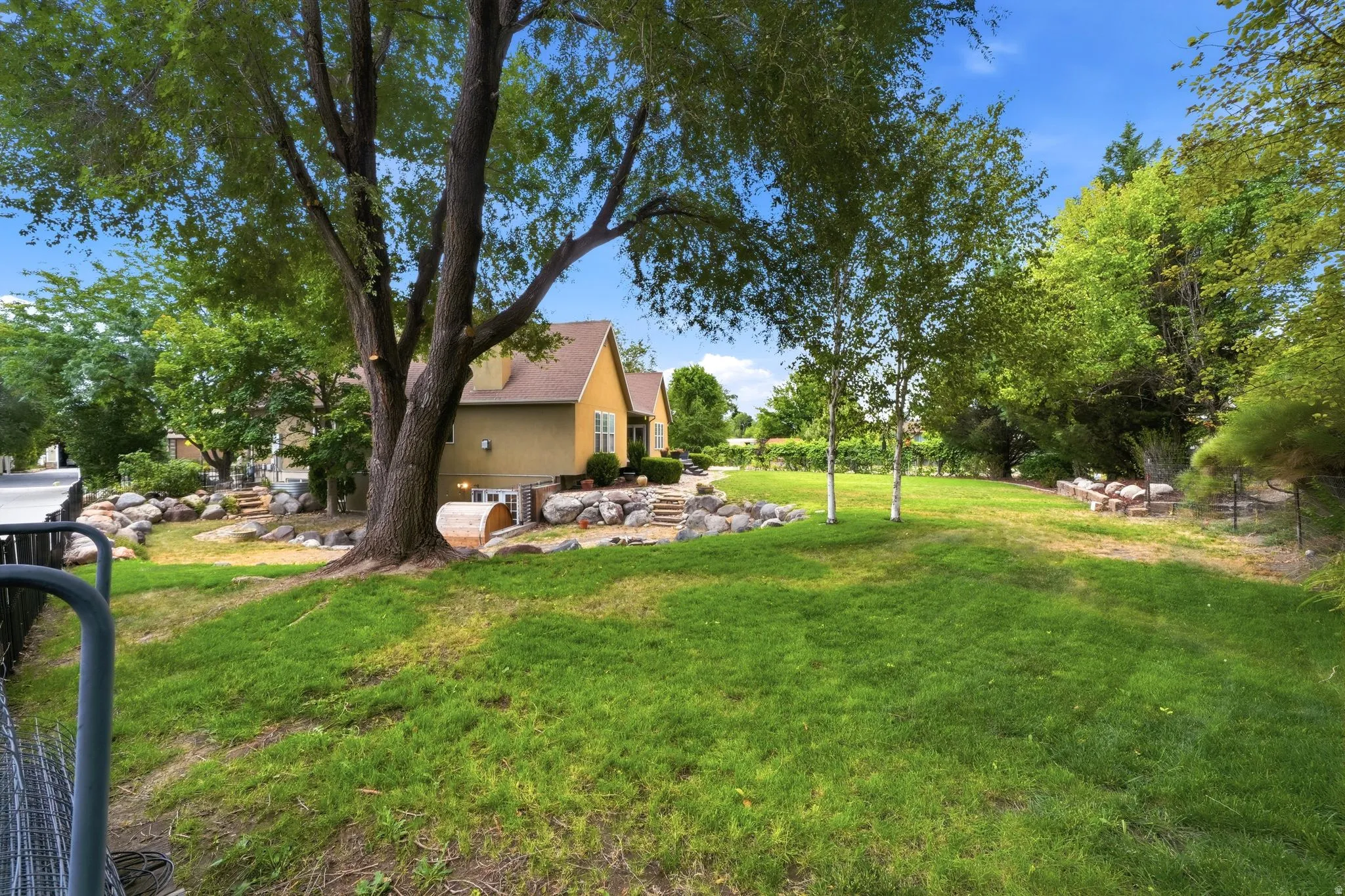 Expansive green lawn with mature trees and natural rock landscaping