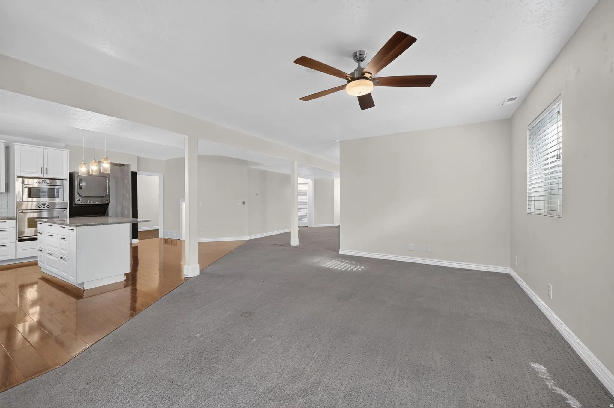 Open-concept living area featuring distinct flooring, a ceiling fan, and a kitchen with white cabinetry, stainless steel appliances, and an island with pendant lighting