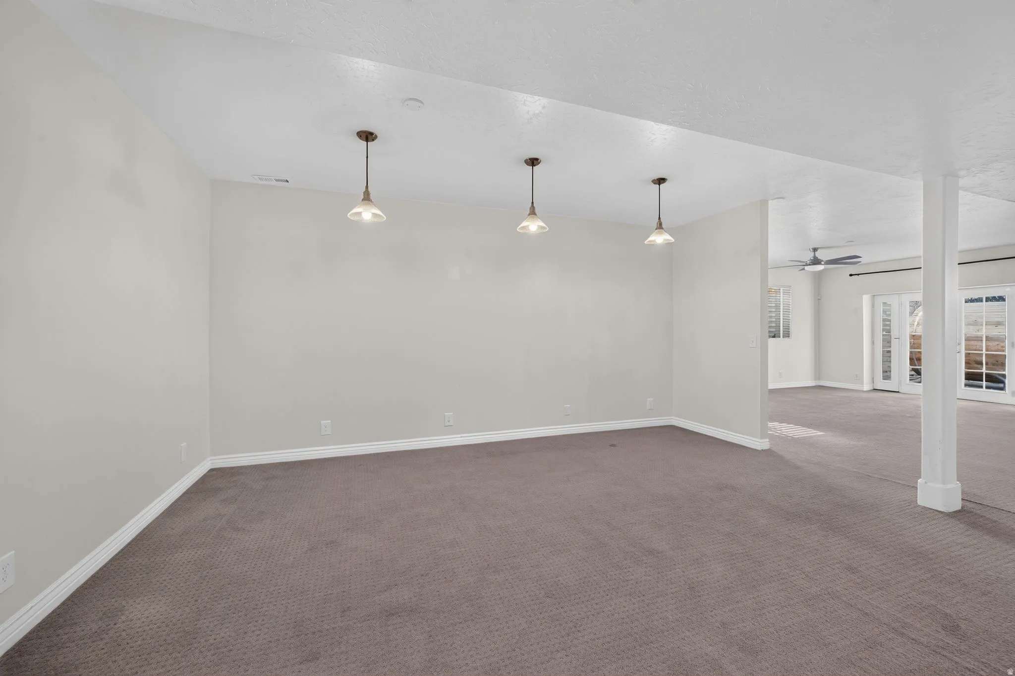 Spacious room featuring neutral carpeting, pendant lighting, and a neutral wall color