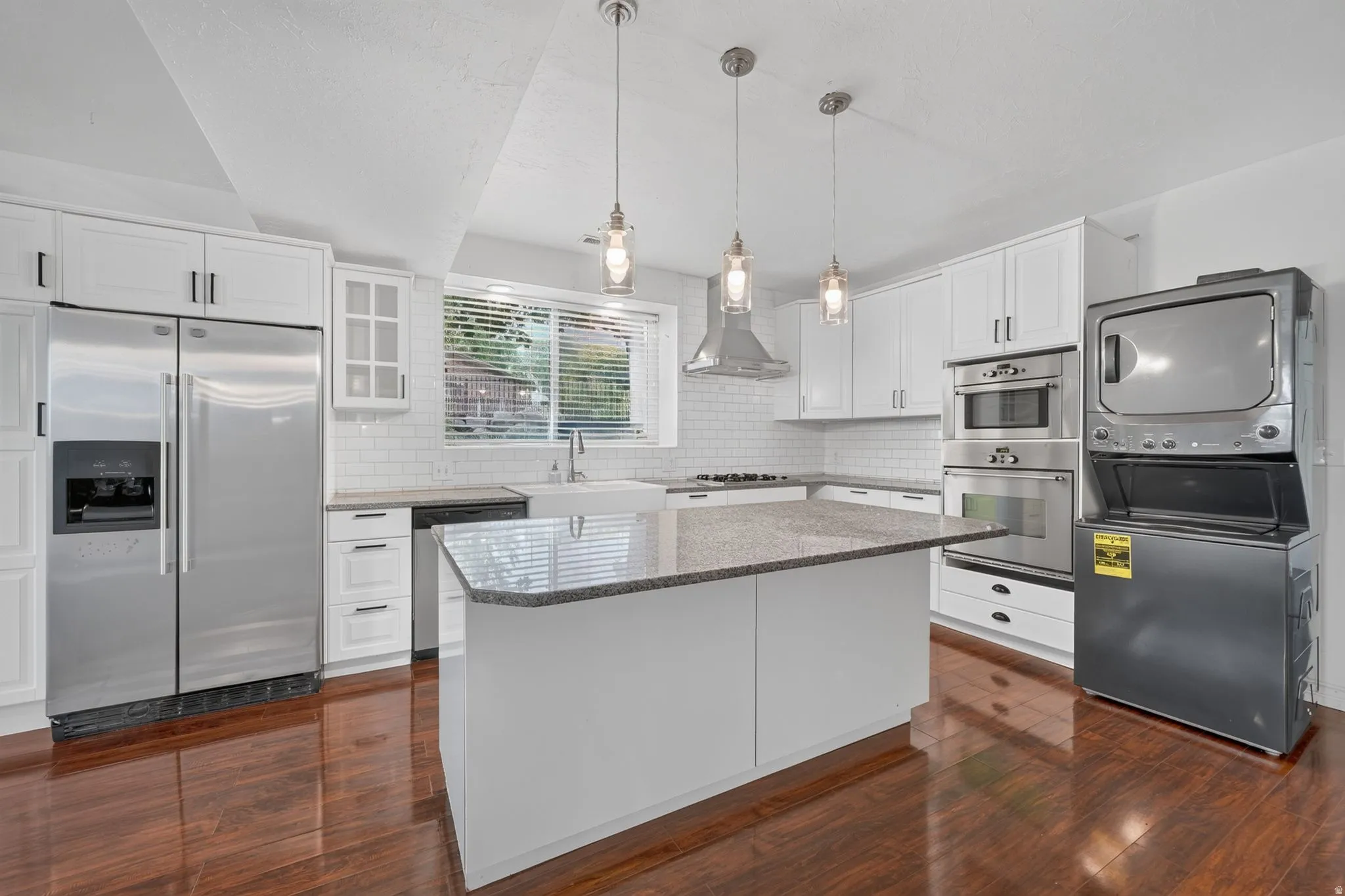 Gourmet kitchen with wood-finish flooring, white cabinetry, a built-in stainless steel appliance suite, granite countertops, and a central island