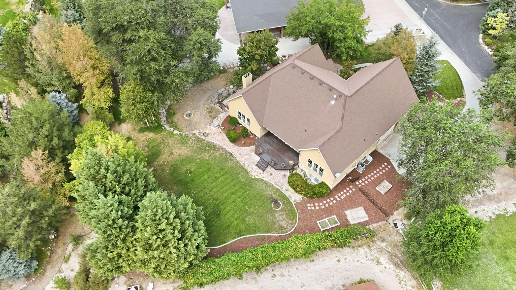 Expansive property featuring a brown shingle roof, yellow siding, a large deck, mature trees, and a manicured lawn