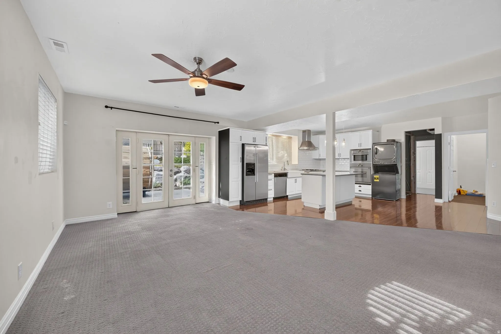 Open-concept living space featuring a ceiling fan, french doors, and carpet flooring