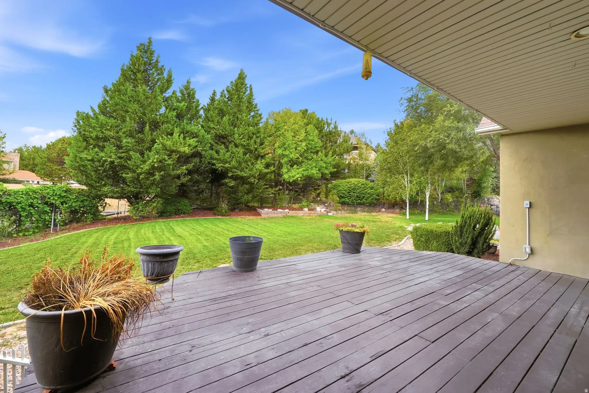 Expansive outdoor deck with a wood-finish surface, overlooking a manicured lawn and mature trees