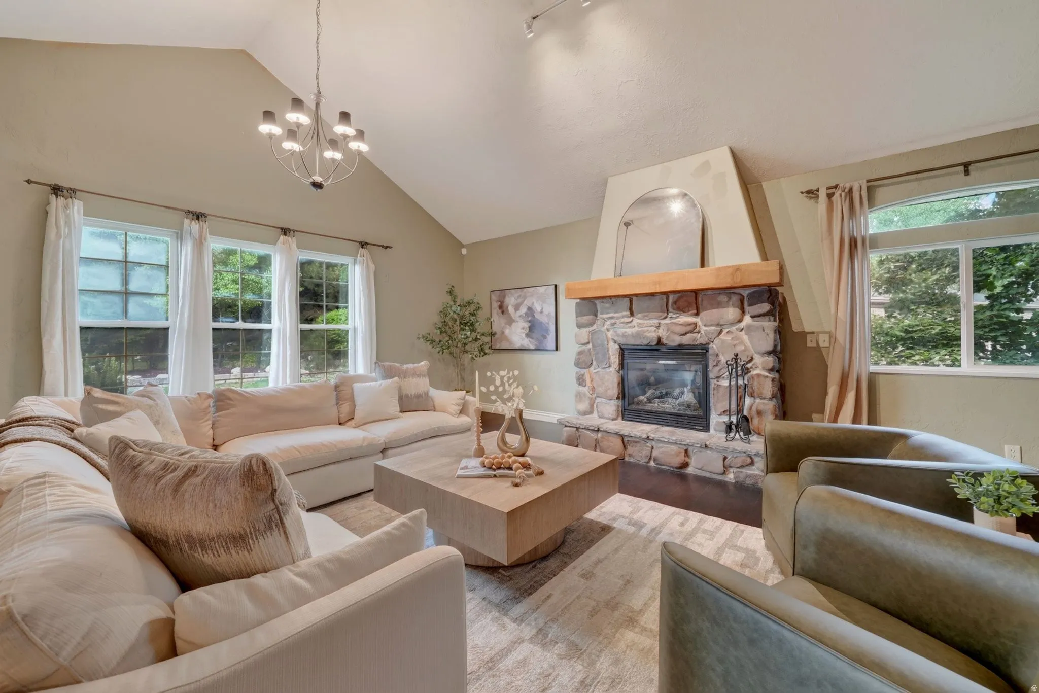 Vaulted ceiling with an attached chandelier, stone-surround fireplace with a wood mantel, and multiple windows