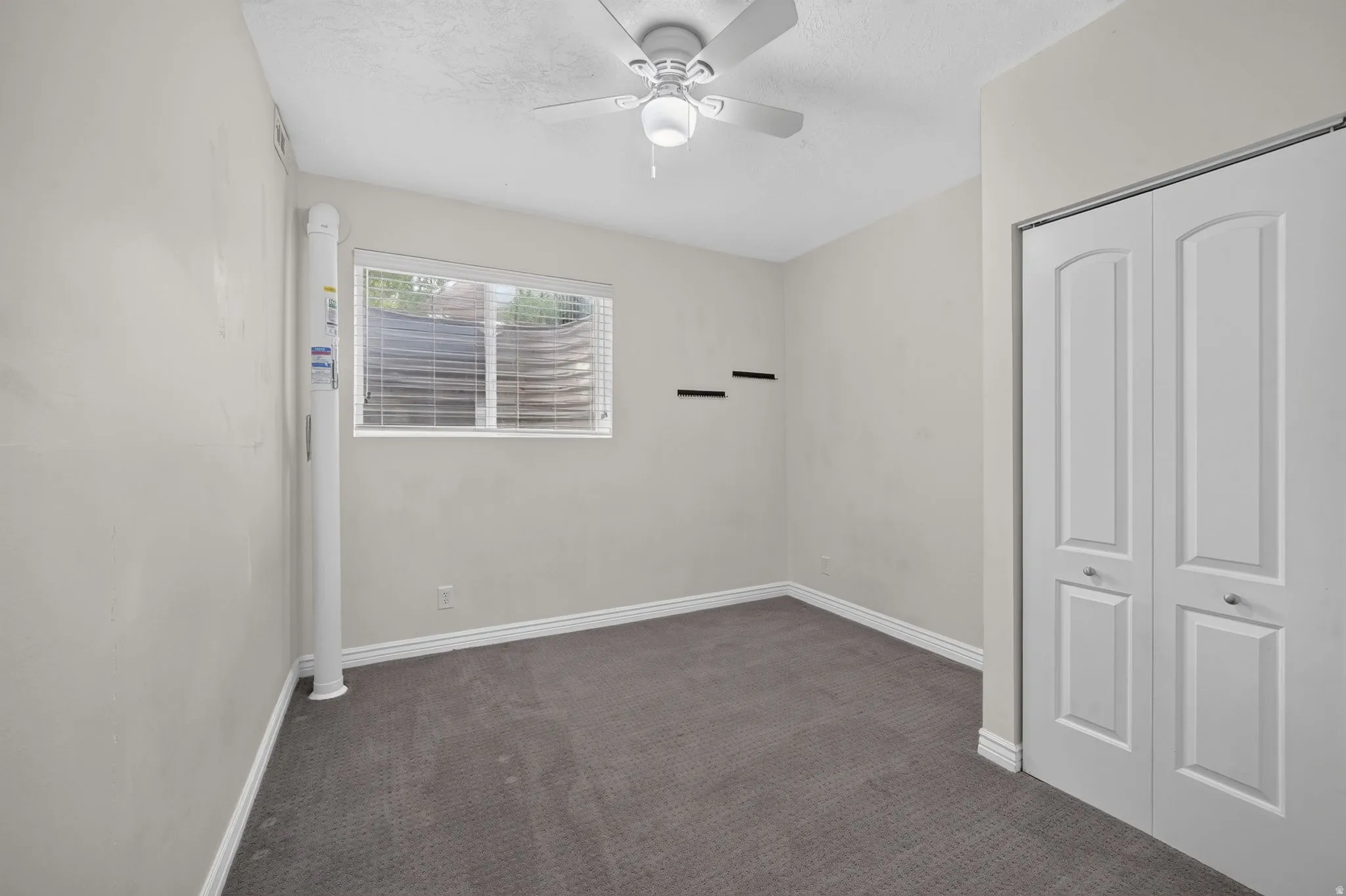 Carpeted flooring, window with blinds, ceiling fan with light fixture, and bi-fold closet doors