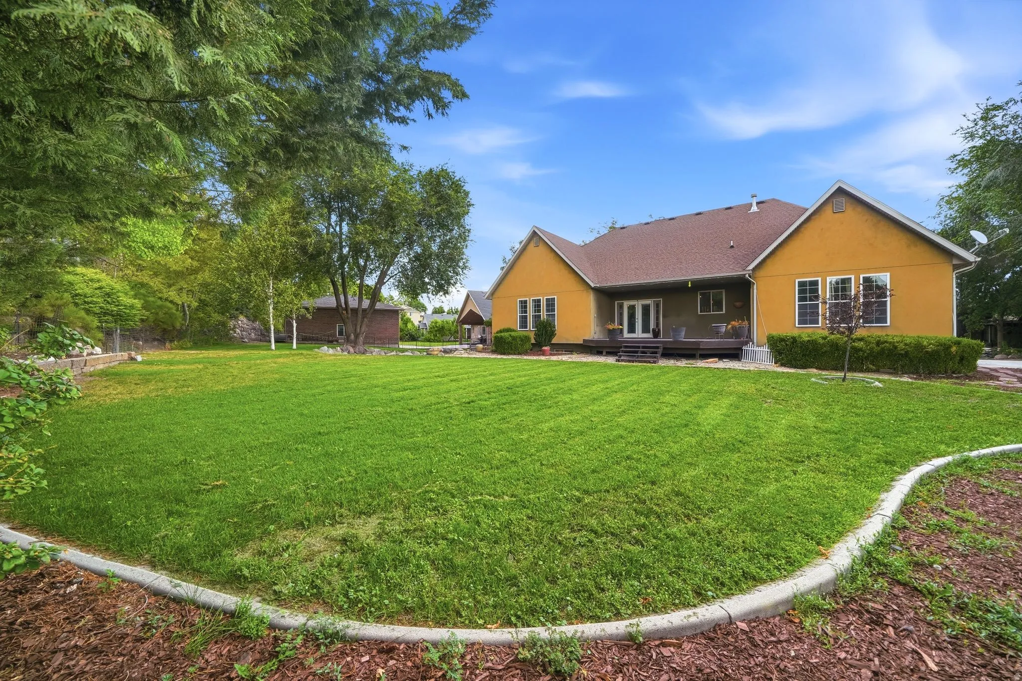 Expansive green lawn with a defined concrete border, mature trees, and a rear deck with direct access to the interior
