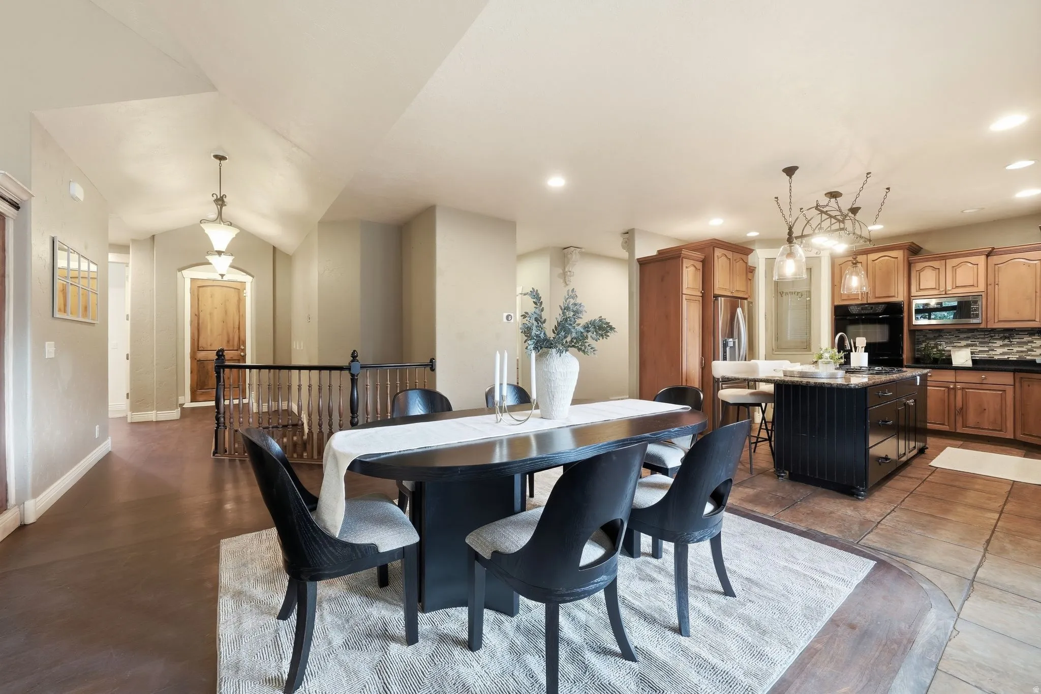 Vaulted ceilings, wood-finish flooring, staircase with wood railing, kitchen island with seating, and wood cabinetry