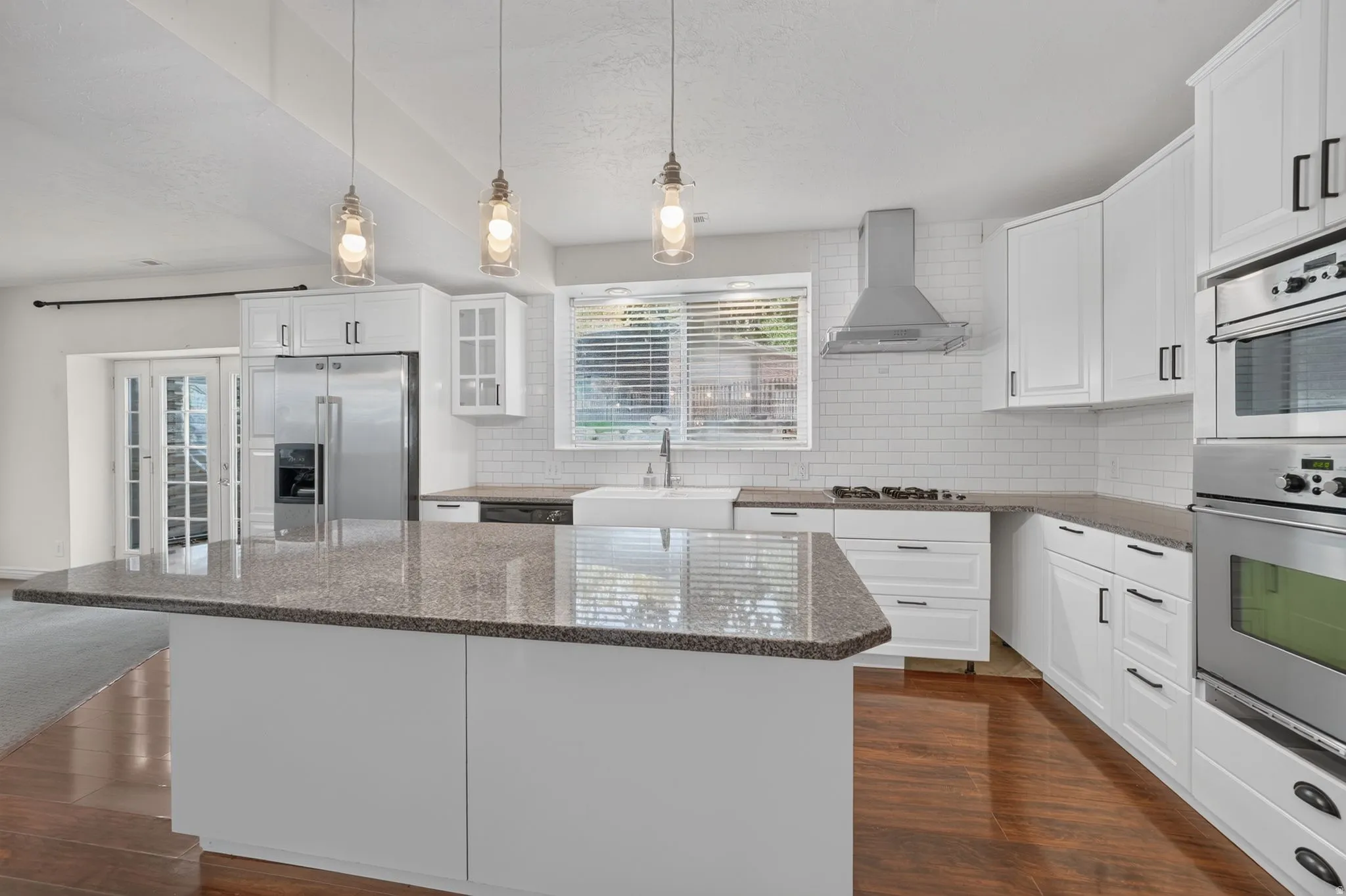 Kitchen featuring white cabinetry, stainless steel appliances, a large island with a stone countertop, and wood-finish flooring