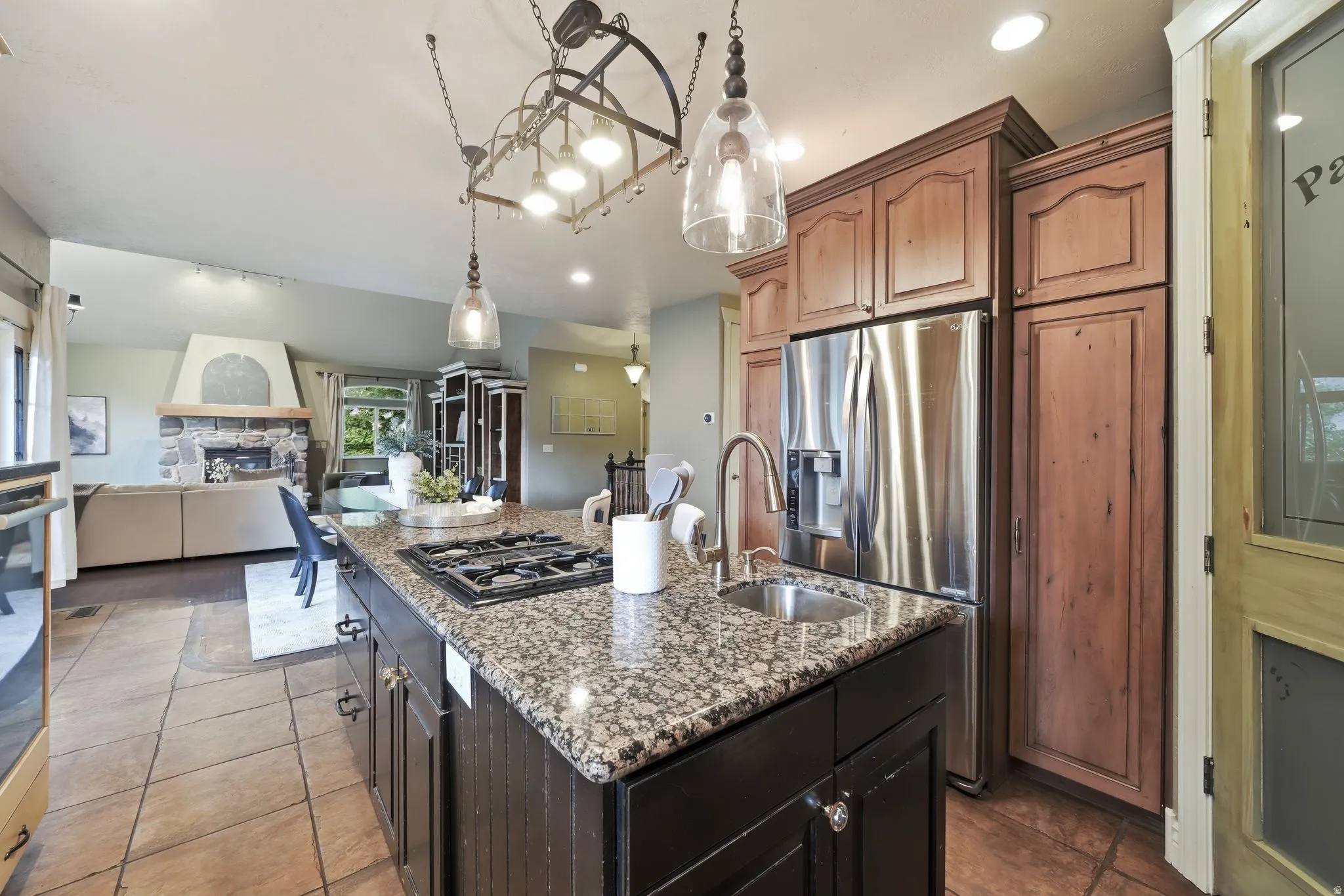 Kitchen island with gas cooktop and undermount sink, granite countertops, and tile flooring