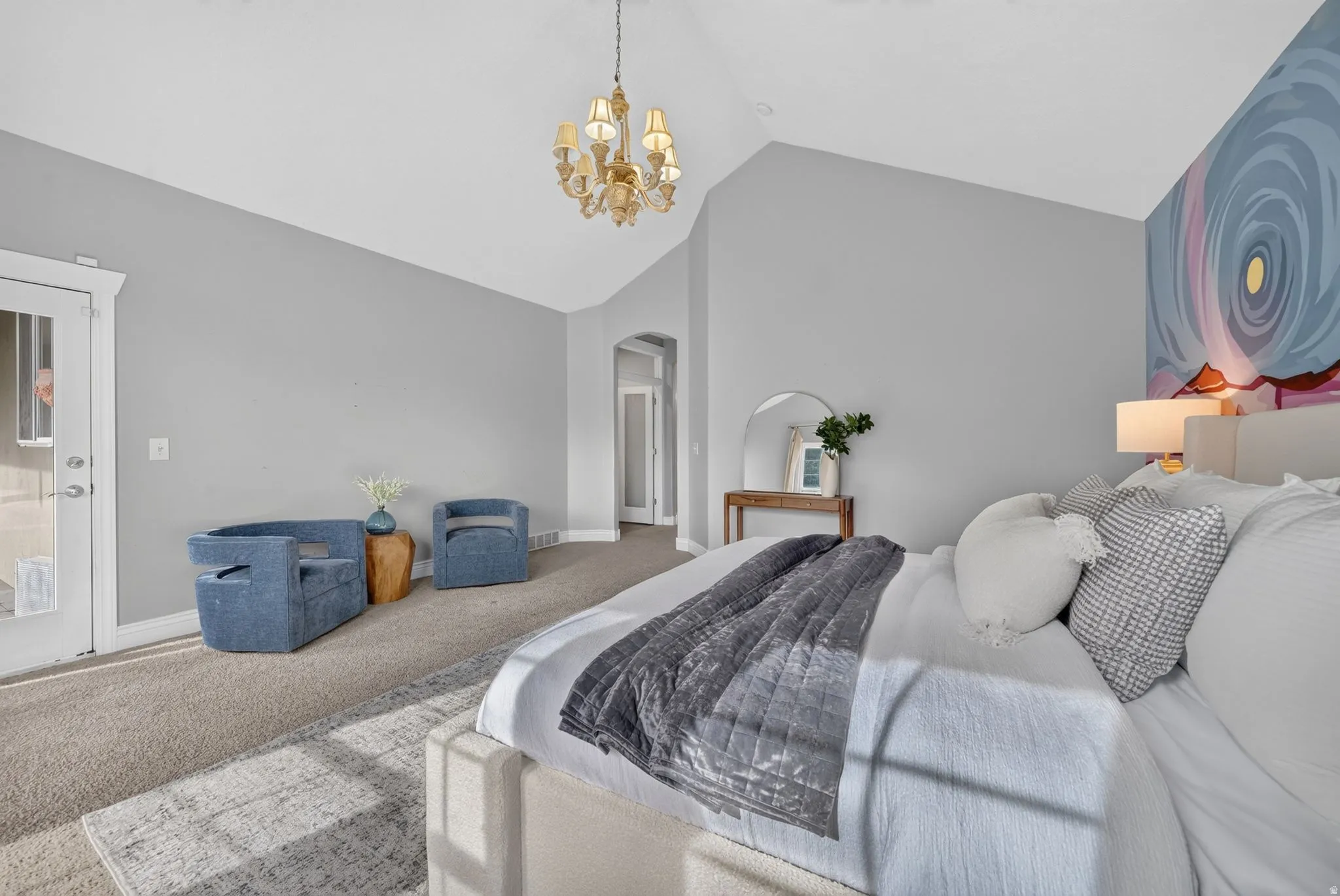 Vaulted ceiling, decorative chandelier, light gray wall paint, arched doorway, and carpet flooring