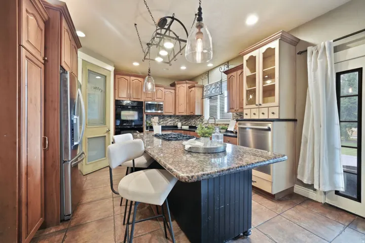 Kitchen featuring an expansive center island with stone countertop, tile flooring, stainless steel appliances, and built-in cabinetry