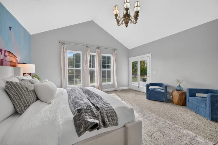 Vaulted ceiling with an ornate chandelier, multiple windows with natural light, and French doors leading to exterior