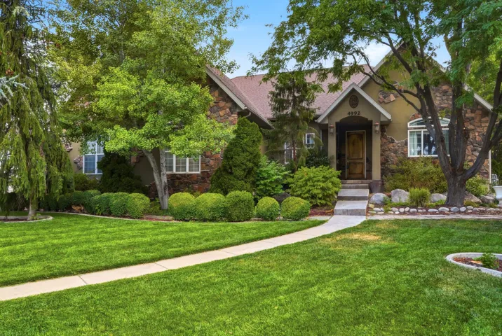 Stone and stucco exterior, prominent entryway, mature trees, manicured lawn, and paved walkway