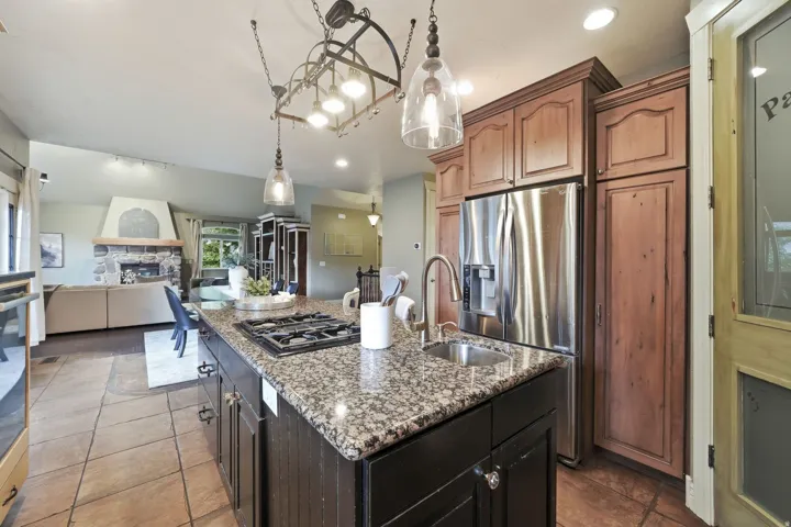 Kitchen island with gas cooktop and undermount sink, granite countertops, and tile flooring