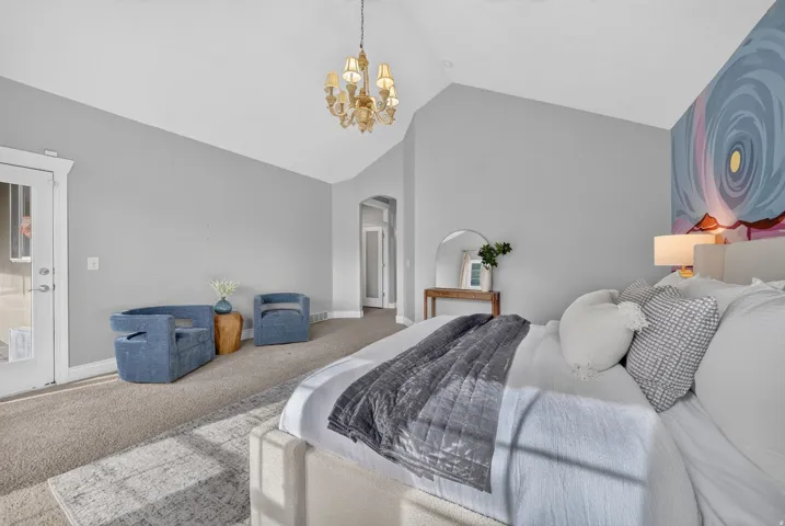 Vaulted ceiling, decorative chandelier, light gray wall paint, arched doorway, and carpet flooring