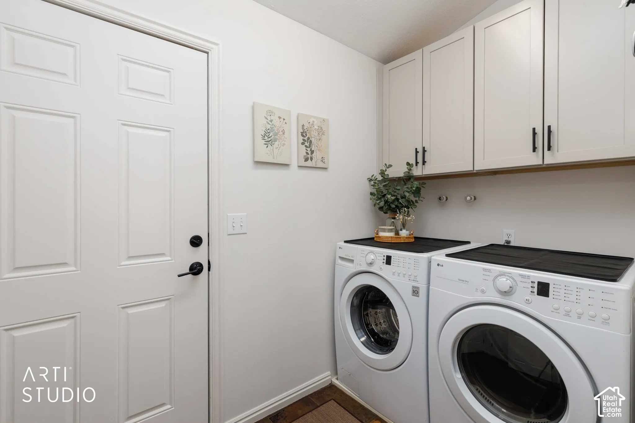 White panel garage door with matte black hardware, Buff Shaker style upper cabinetry with matte black pulls, and white wall featuring washer and dryer