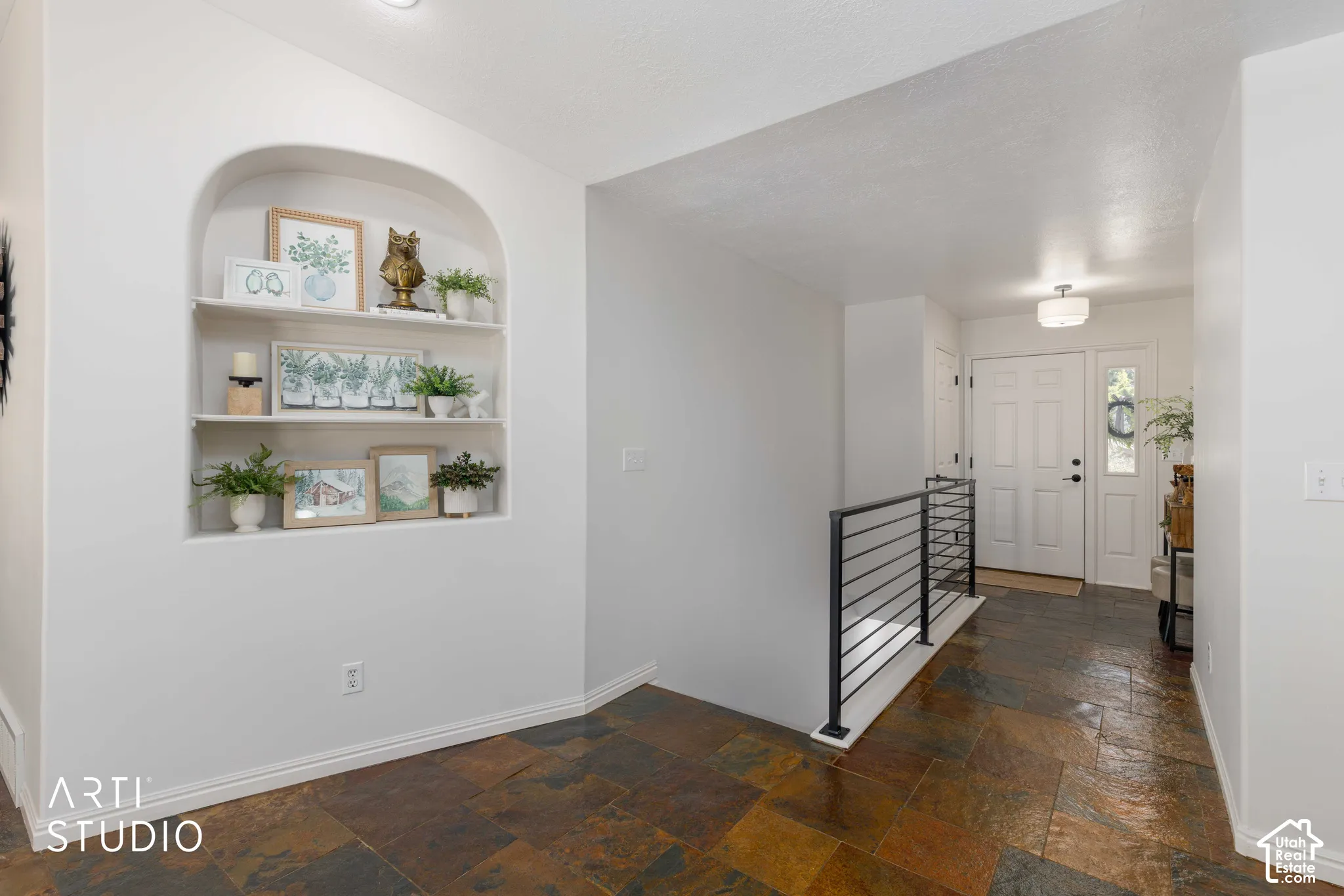 Arched built-in shelving, multi-tone slate tile flooring, white entry door with frosted glass sidelight, black metal horizontal railing, and a semi-flush mount ceiling light fixture