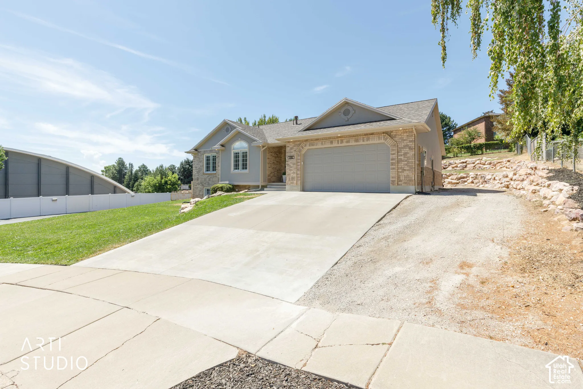 Welcoming home featuring a two-car attached garage with concrete driveway, brick and stucco exterior, pitched roofline with gabled design, and expansive front lawn with mature landscaping