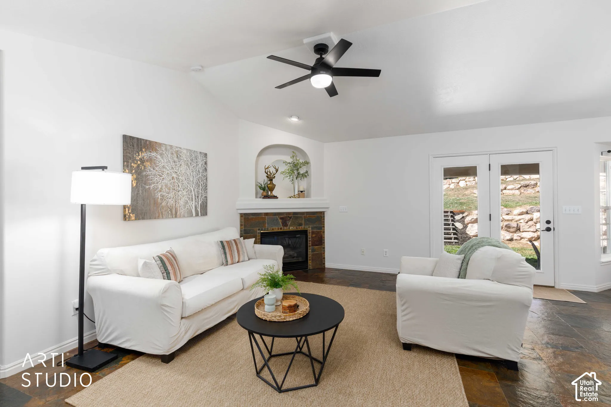 Vaulted ceiling with a ceiling fan, stone-clad fireplace with an arched alcove, double glass-paneled doors, and multi-toned slate flooring