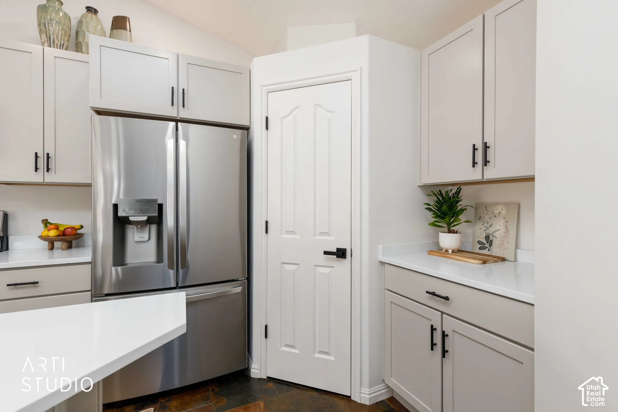 Stainless steel refrigerator, Buff shaker-style cabinetry, white quartz countertops, corner food pantry, and new black hardware