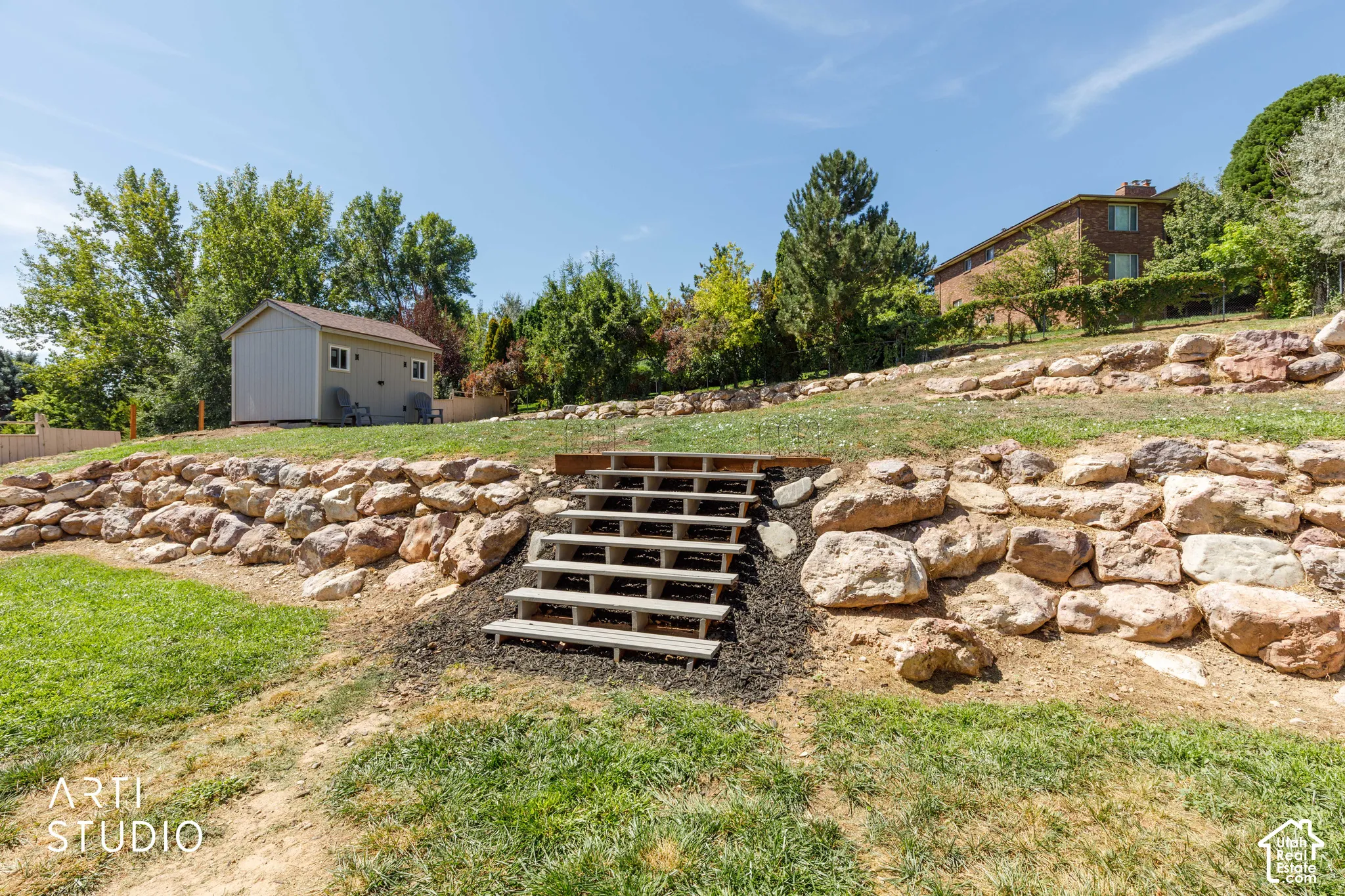 Tiered landscaping with rock retaining walls, wooden steps, and newer shed.