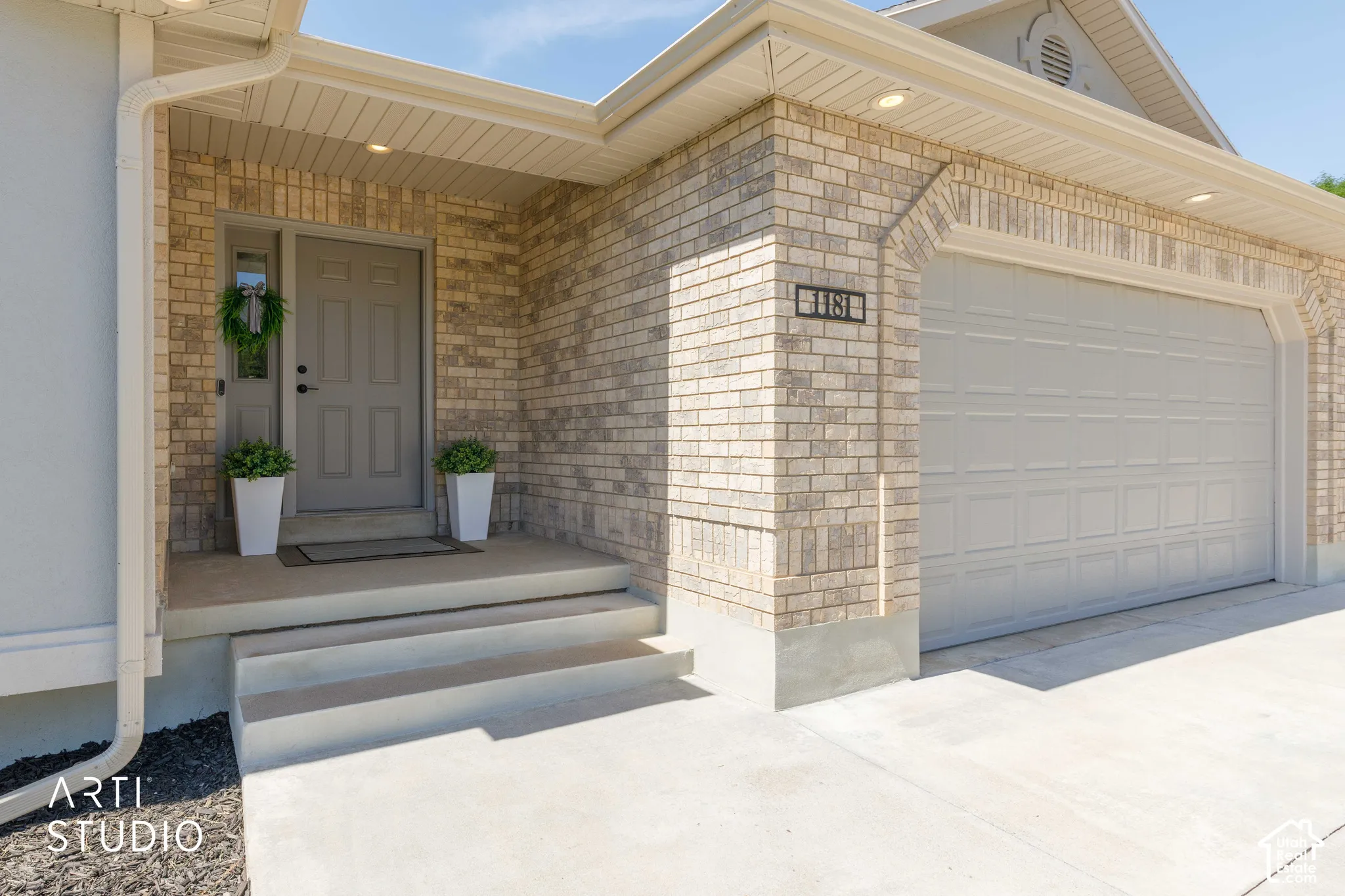 Brick exterior with arched garage door surround, concrete driveway, concrete porch, and multiple recessed soffit lights
