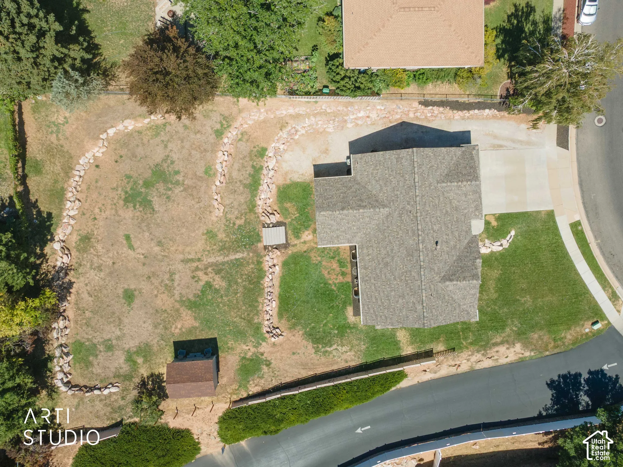 Expansive property .43 featuring a shingled roof, paved driveway, storage shed, and rock landscaping elements