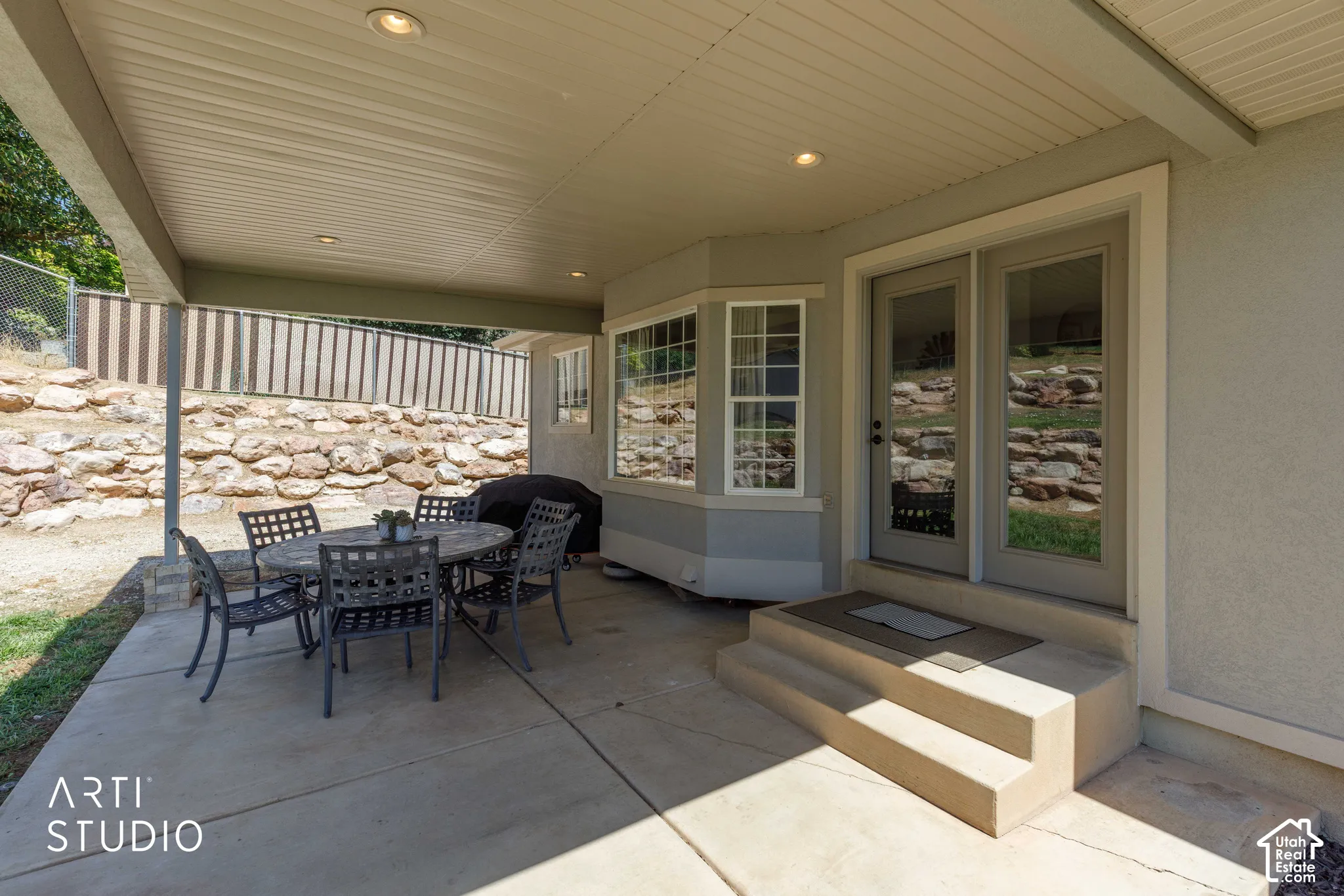 Covered concrete patio with recessed lighting and box bay window and stairs leading from interior family room.