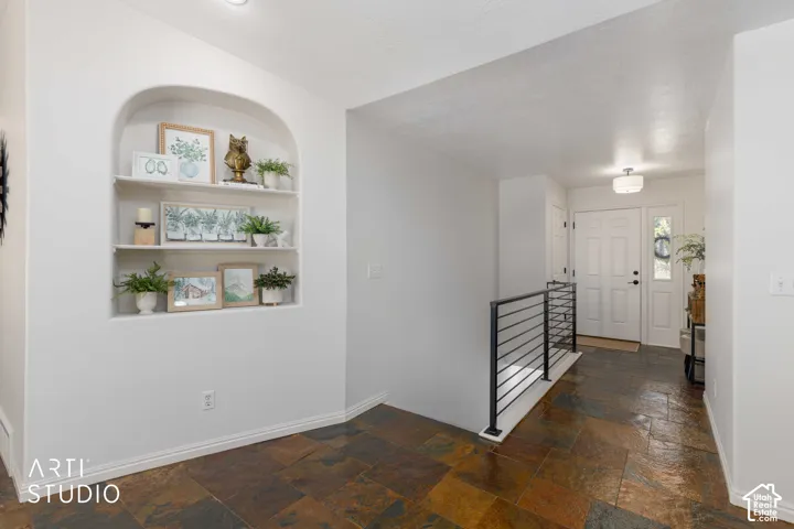 Arched built-in shelving, multi-tone slate tile flooring, white entry door with frosted glass sidelight, black metal horizontal railing, and a semi-flush mount ceiling light fixture