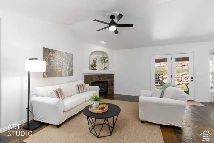 Vaulted ceiling with a ceiling fan, stone-clad fireplace with an arched alcove, double glass-paneled doors, and multi-toned slate flooring
