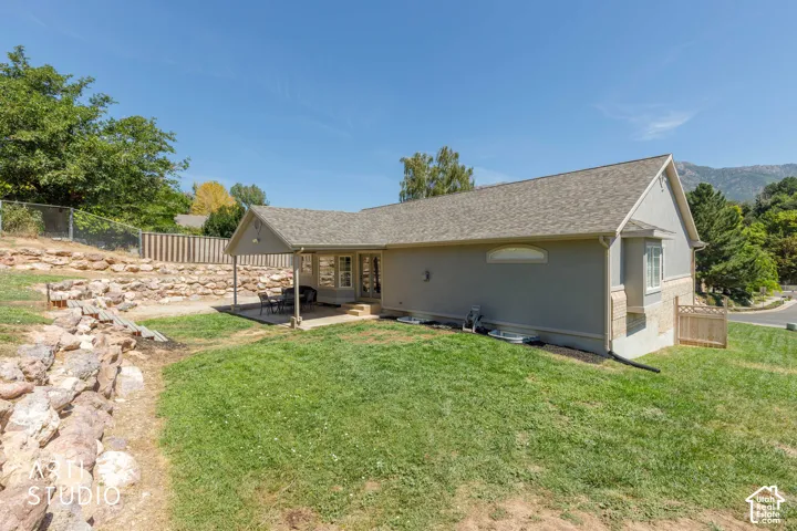 Side yard view featuring a covered patio, terraced rock landscaping, and a partial fenced perimeter
