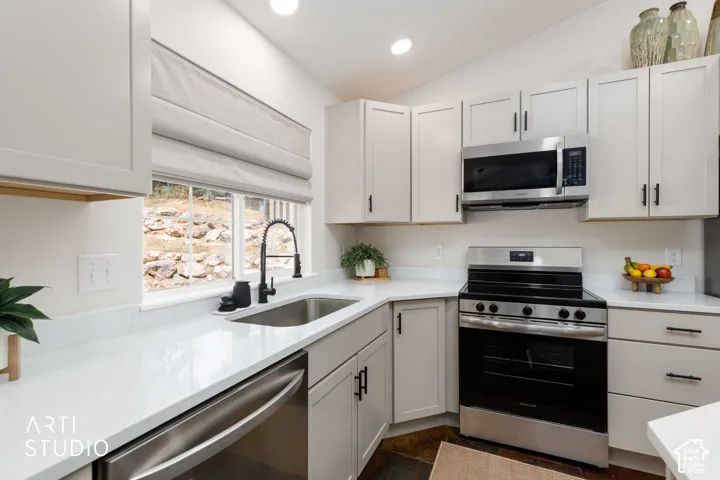 Kitchen featuring Buff  cabinetry, white quartz countertops, newer stainless steel appliances, a black gooseneck faucet, and slate tile flooring