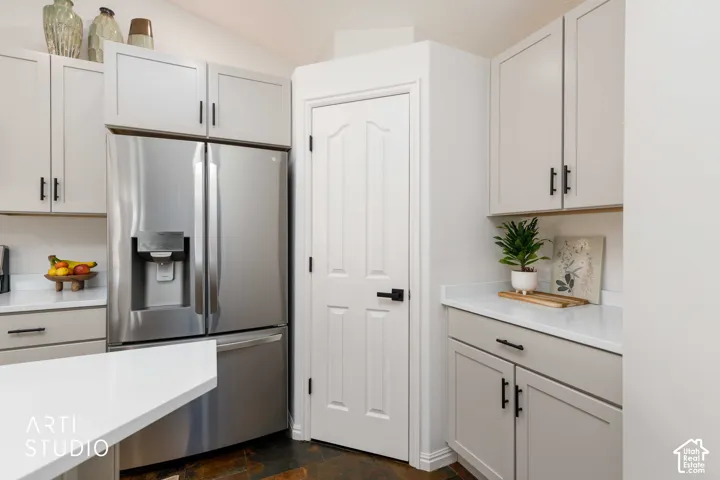 Stainless steel refrigerator, Buff shaker-style cabinetry, white quartz countertops, corner food pantry, and new black hardware
