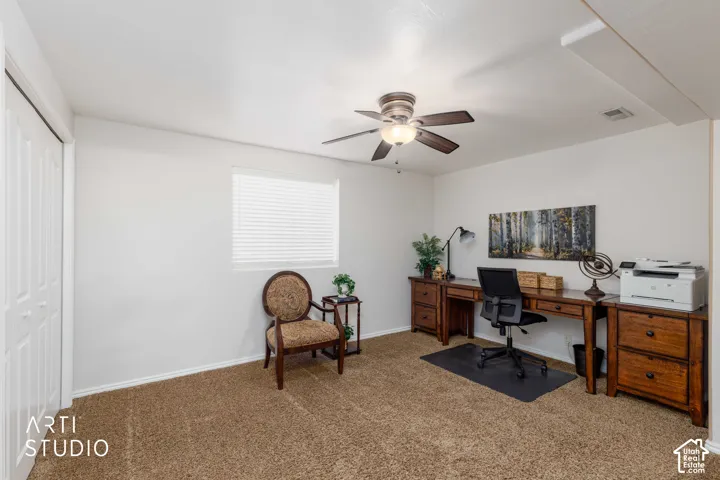 Bedroom #6 staged as office with ceiling fan with integrated lighting, window with white blinds, bi-fold closet doors, wall-to-wall brown carpeting, and partial tan accent wall.