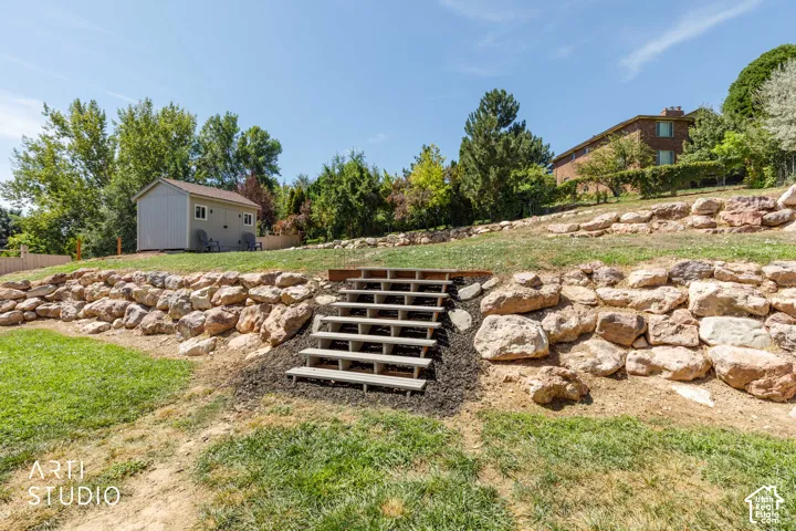 Tiered landscaping with rock retaining walls, wooden steps, and newer shed.