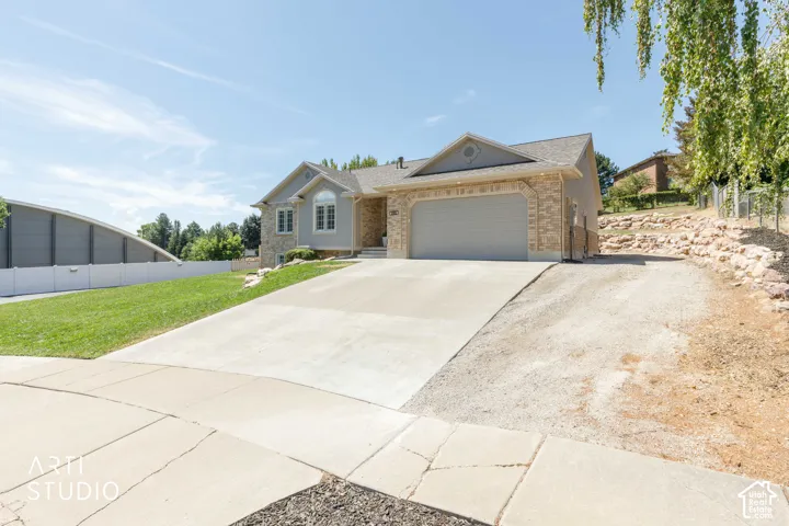 Welcoming home featuring a two-car attached garage with concrete driveway, brick and stucco exterior, pitched roofline with gabled design, and expansive front lawn with mature landscaping