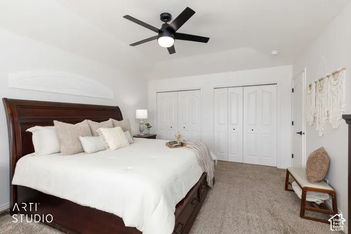 large bedroom with Vaulted ceiling, New ceiling fan with integrated lighting, two sets of bi-fold closet doors, and new tan carpeted flooring. Features a king size bed in room.