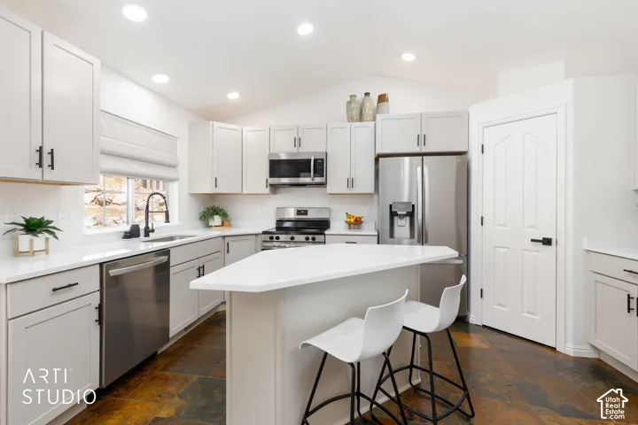 Modern kitchen featuring New Buff  Shaker style cabinetry, stainless steel appliances, a center island with quartz countertop seating, recessed lighting, and multi-toned slate  tile flooring