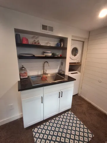 Integrated kitchenette with stainless steel sink, dark countertop, and white cabinetry